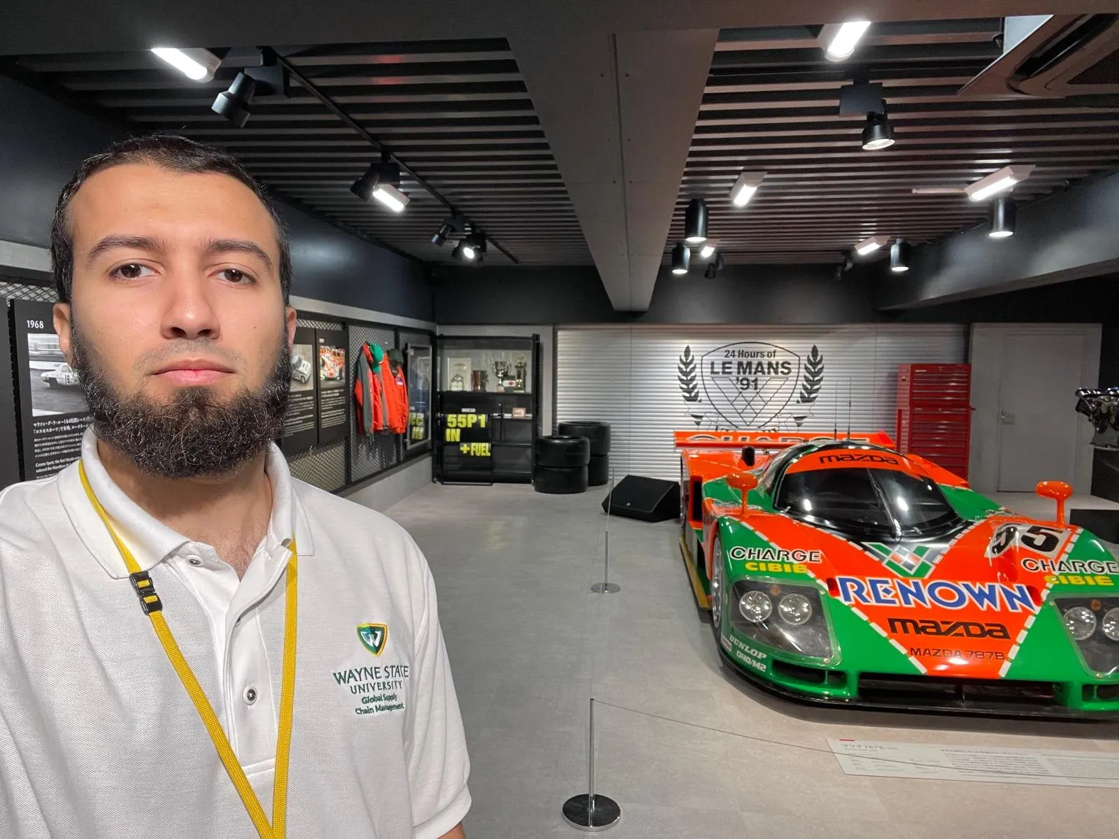 Gotibeh in a Wayne State polo at the Mazda Museum in Hiroshima with the green and orange Mazda 787B Le Mans car behind him.
