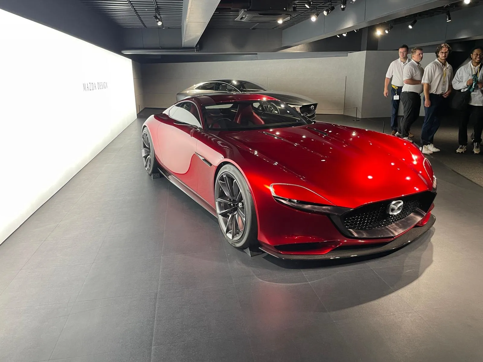 A deep red Mazda RX-Vision concept car under spotlights in the Mazda design hall.