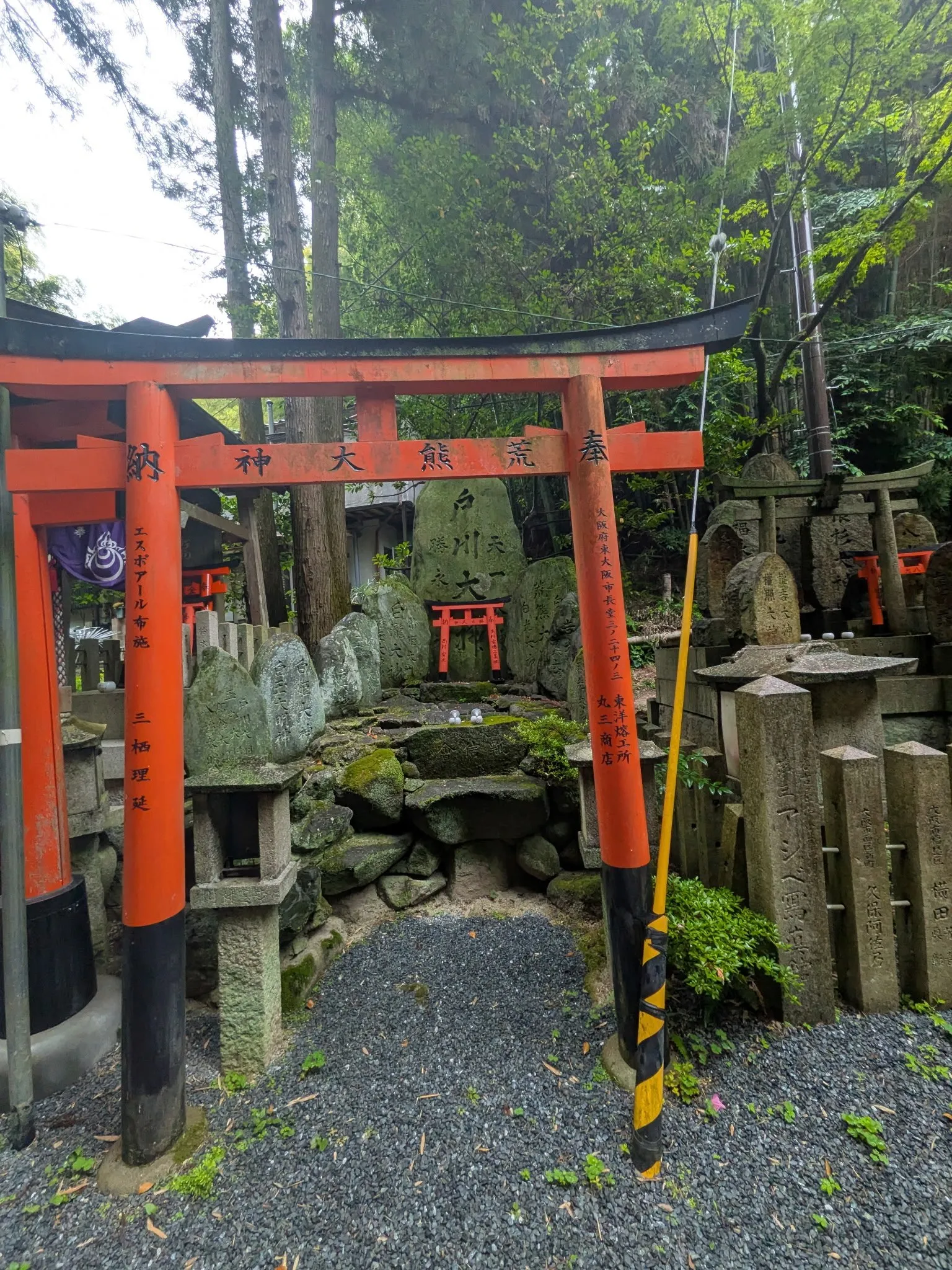 A path at Fushimi Inari running under vermilion torii gates, with weathered stone shrine markers and miniature gates stacked along the side.