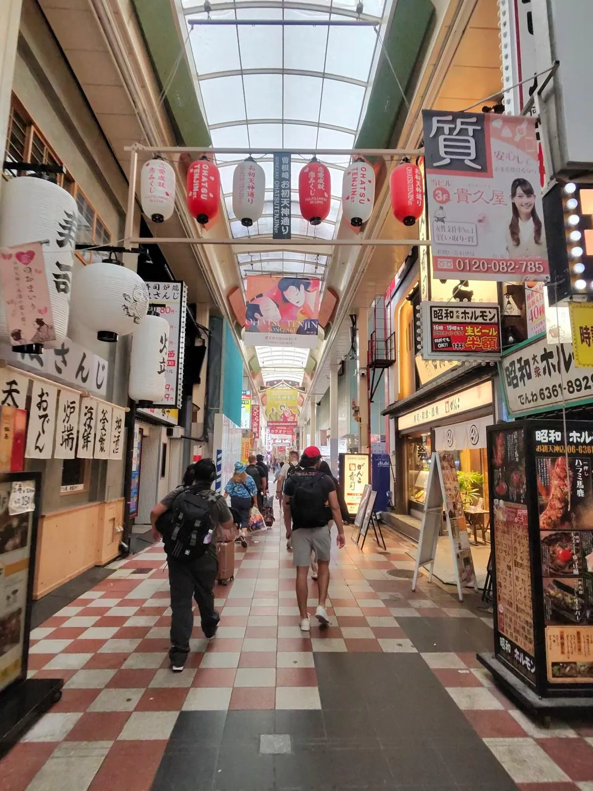 A long covered shopping arcade in Osaka with a chequered floor and shopfronts receding into the distance.