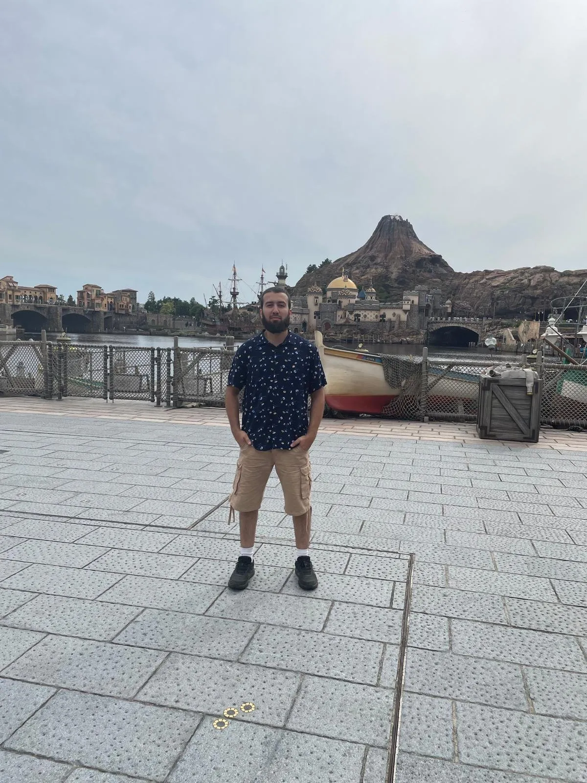 Gotibeh standing on the waterfront promenade at Tokyo DisneySea with the volcano of Mysterious Island rising behind him.