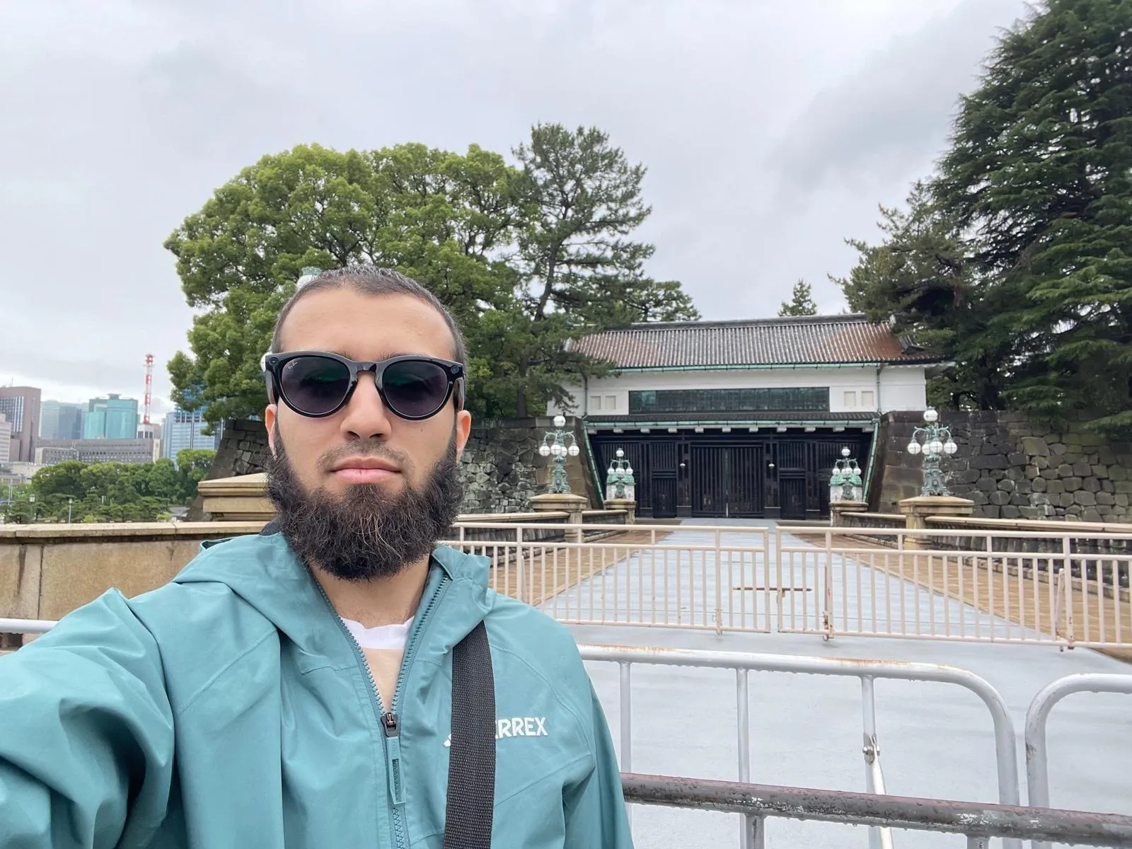 Gotibeh in a teal jacket and sunglasses in front of a dark wooden gate at the Imperial Palace grounds.