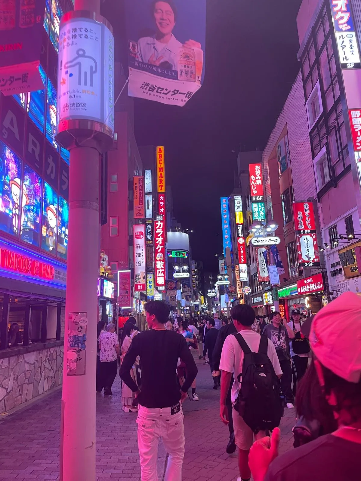 A Tokyo street at night lit by pink and blue neon signs, with people walking under the shopfronts.