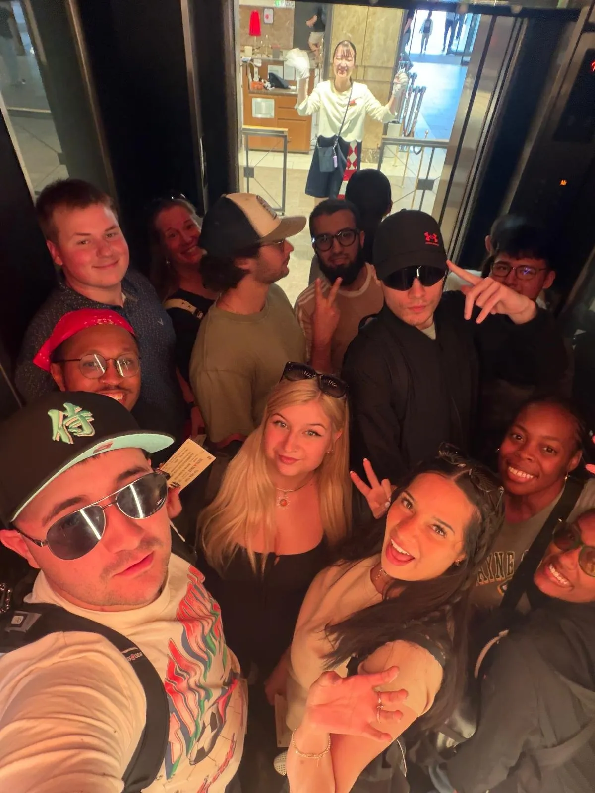Classmates crowded into a lift, faces lit from above, on the way up Tokyo Tower.